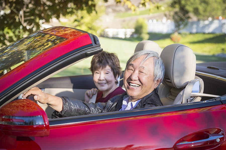 Client Center - Senior Couple in a Red Convertible, Smiling, Surrounded by Greenery