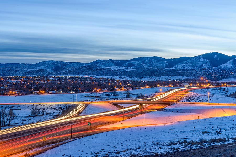 Littleton, CO Insurance - Long Exposure of Denver, Colorado at Night, Traffic Rushing By, Homes Lit up for the Evening, Snow Covered Mountains Above